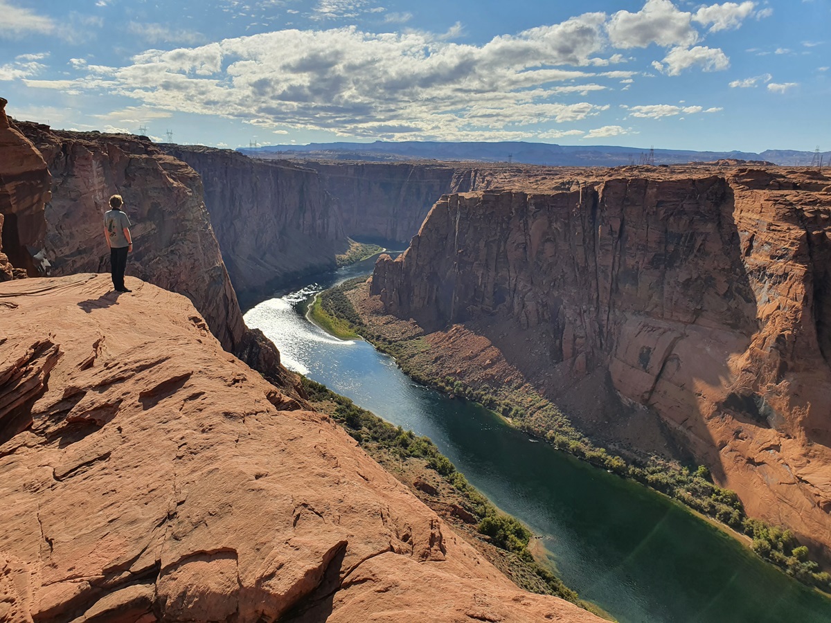 A person standing at the scenic overlook above Horseshoe Bend with the river far below.