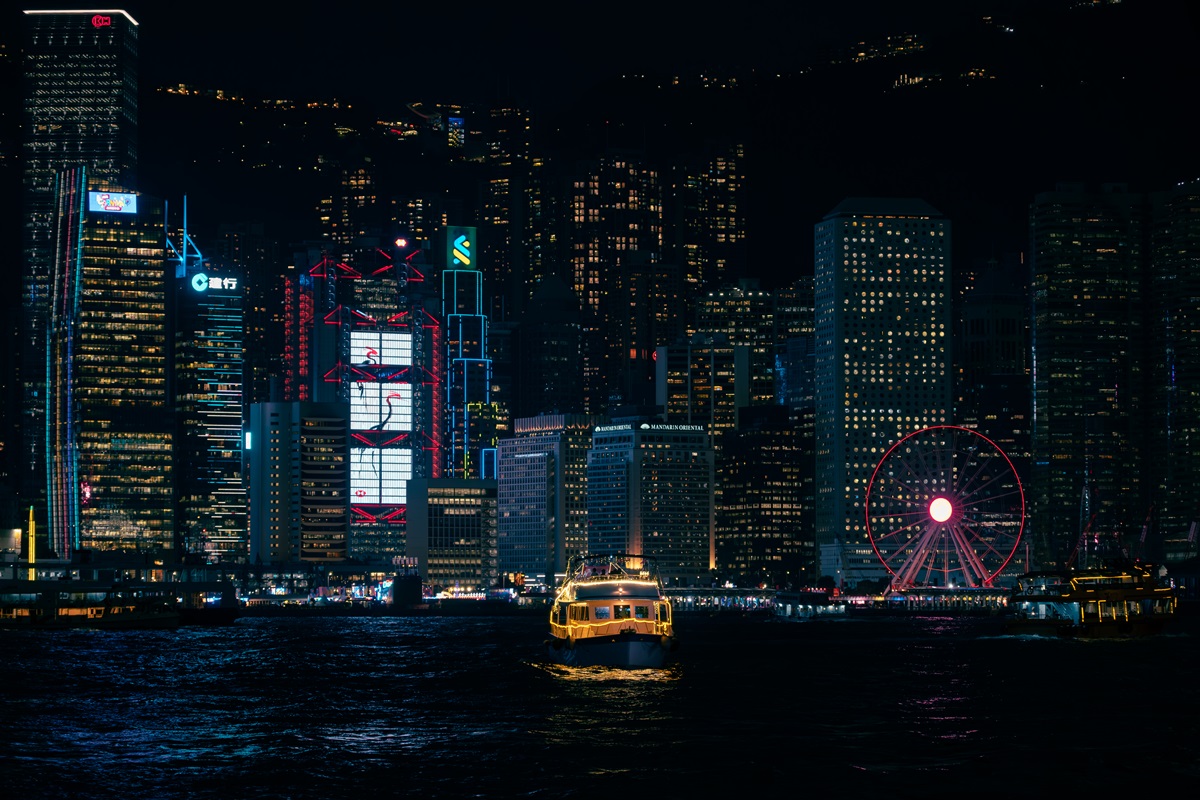 A yellow boat with yellow neon lighting crossing the Victoria Harbour in Hong Kong at night, with lit up sky scrapers in the background.