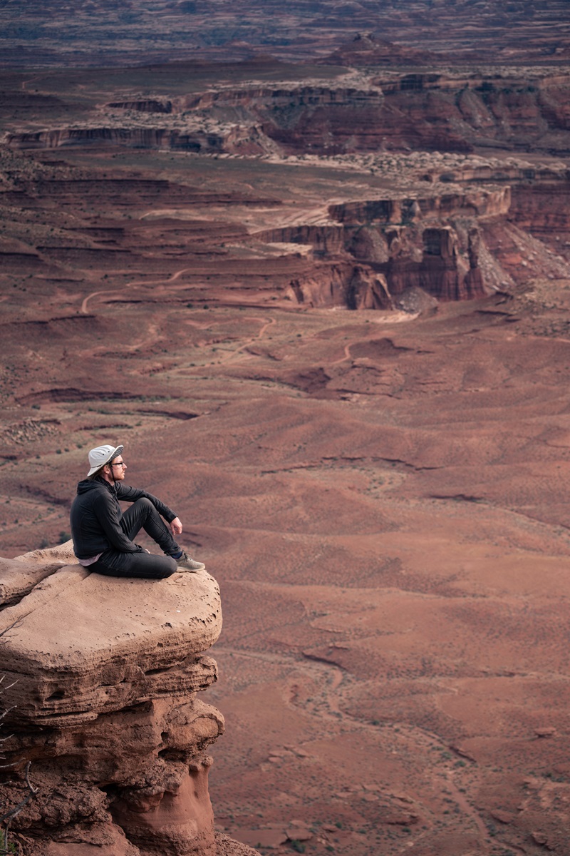 A person sat on a rocky outcrop high above the White Rim Trail at Murphy Point.