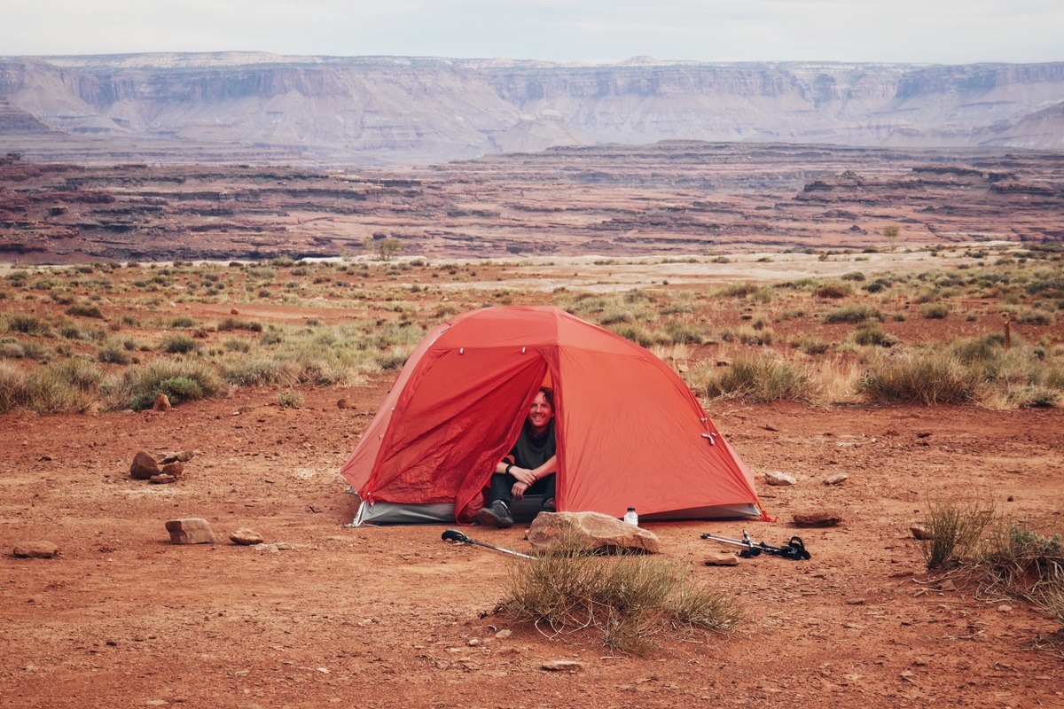 A person sat inside their orange tent, smiling out under grey skies at Canyonlands National Park.
