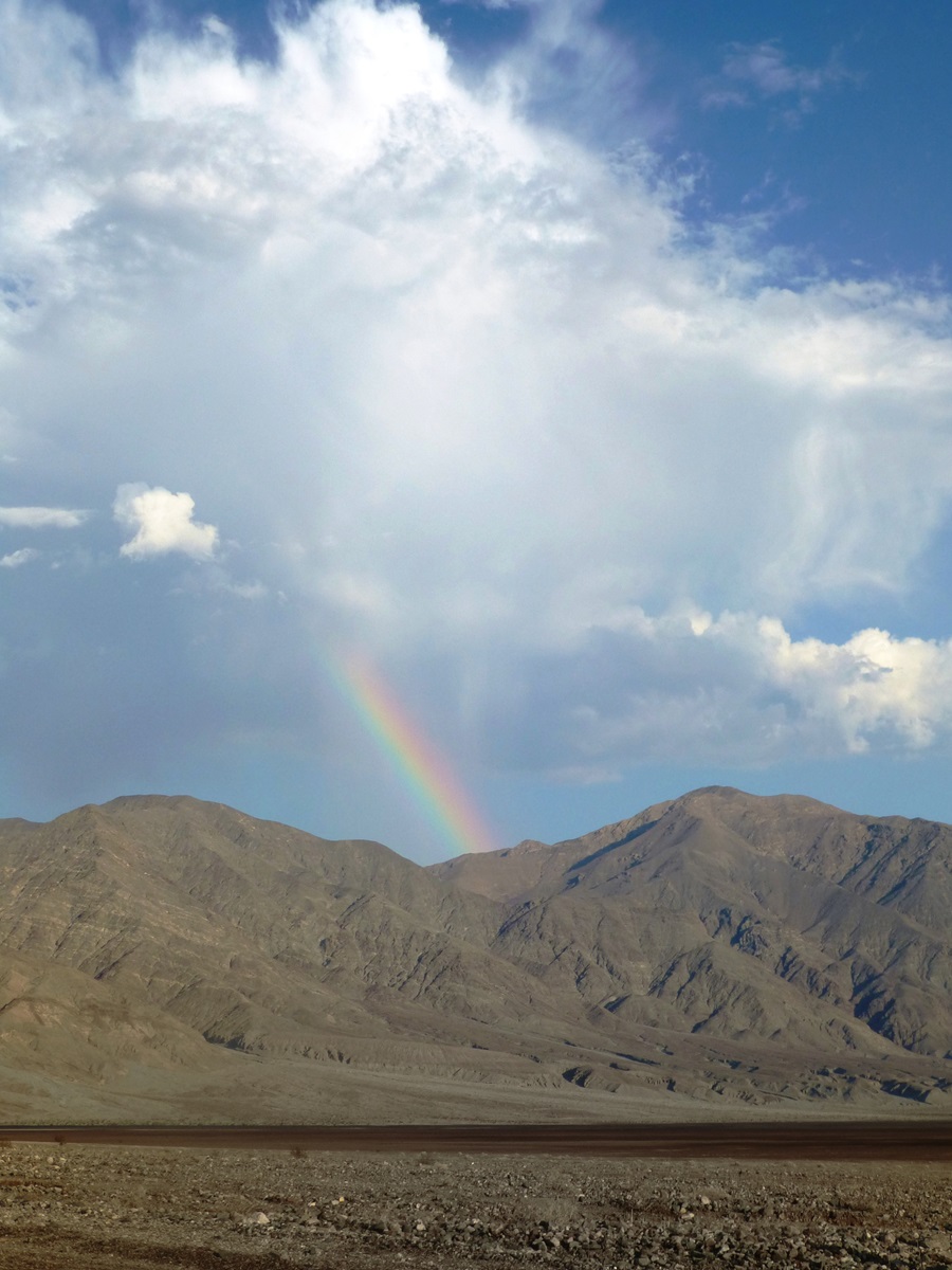 A rainbow appearing above the rocky mountain surroundings of Death Valley in California.