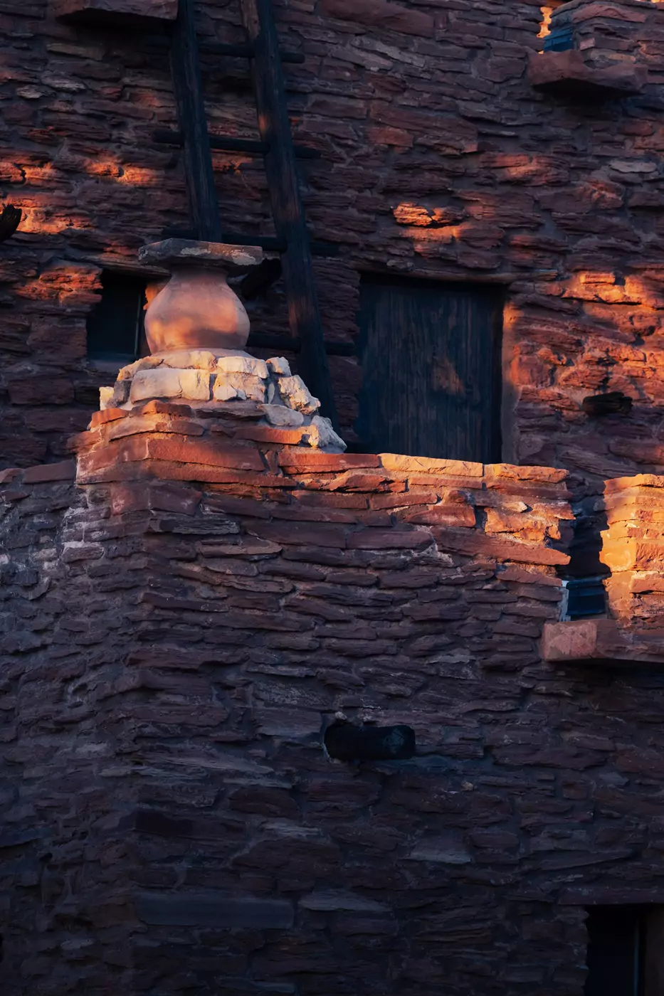 Earthen pot on a stone ledge of a Native American rustic brick building, during sunset.