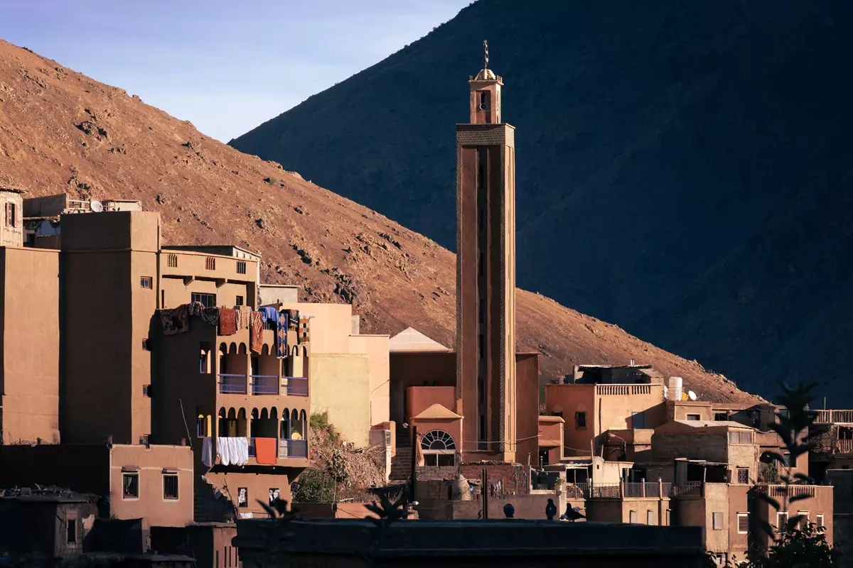 A tall mosque minaret in Imlil, Morocco in the later afternoon sunshine, backed by hills