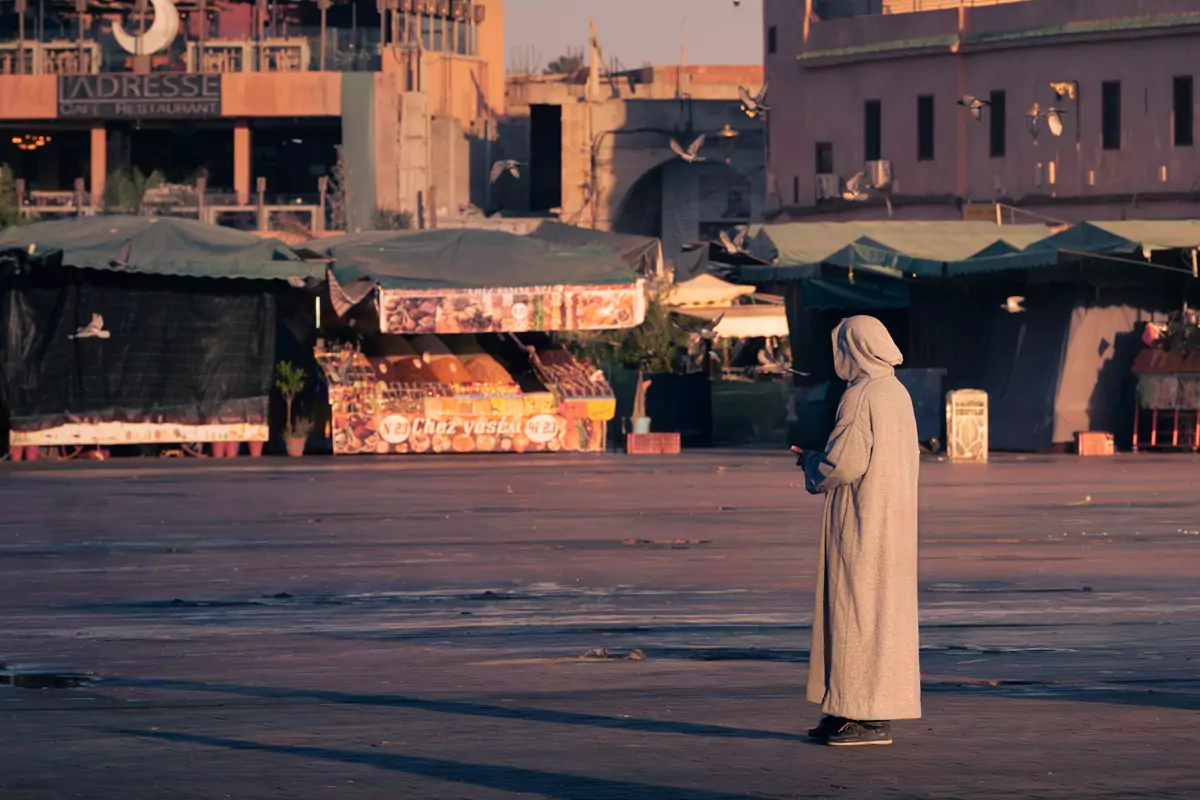 A person at sunrise in a white robe standing in the main square of Jamaa El Fna, Marrakech.
