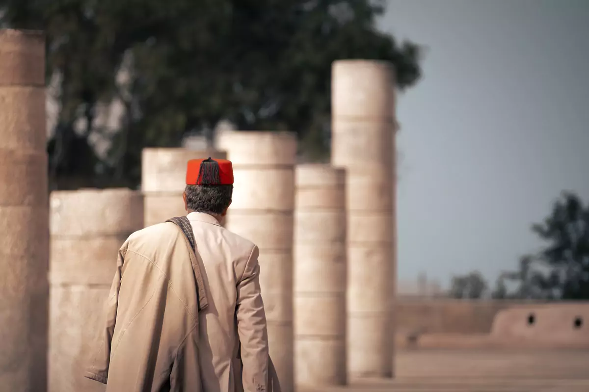 A person wearing a red fez and a tan suit, walking through Rabat in Morocco.