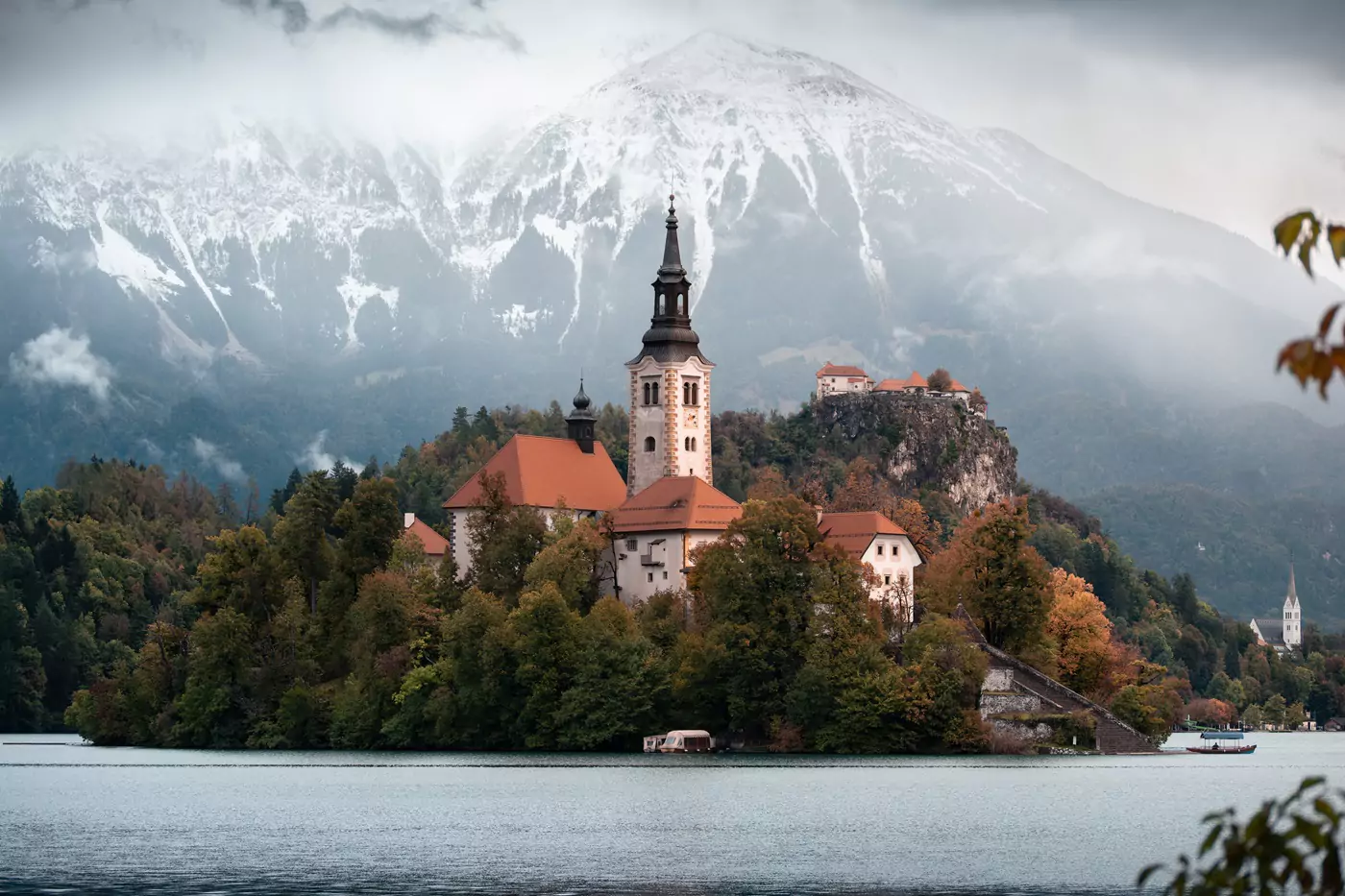 Church Of The Assumption in the centre of Lake Bled with snow peaked mountains in the background.
