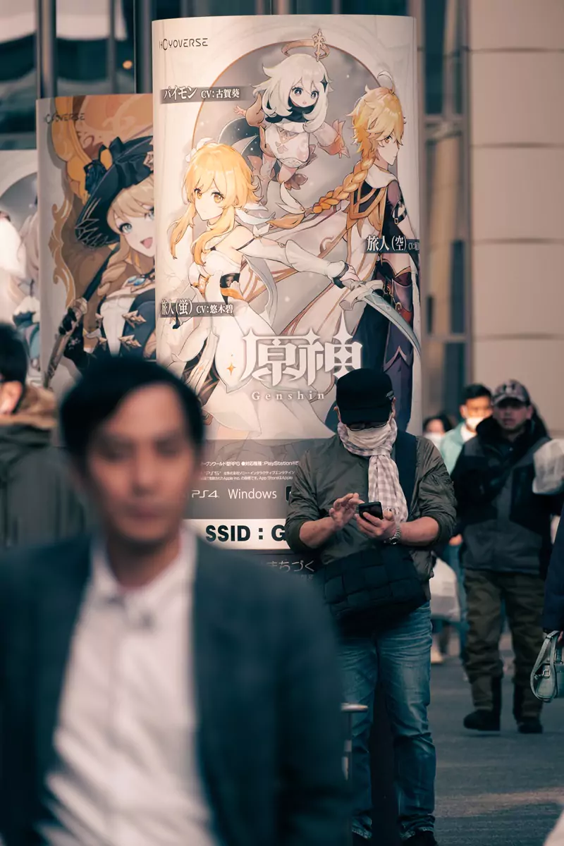 A person on their phone, leaning against a pillow with a poster advertising a new video game in Tokyo, Japan