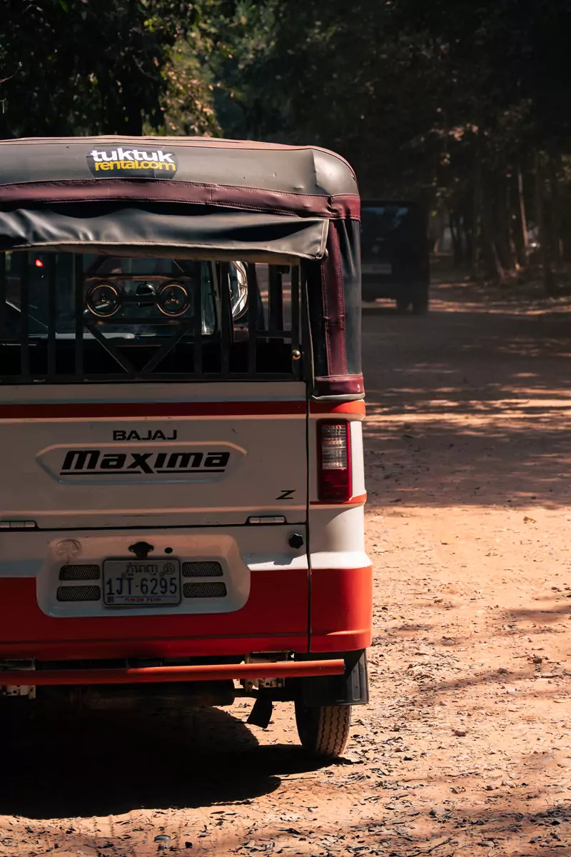 An orange and white rental tuktuk parked on a dusty side track in Angkor Wat, Siem Reap.
