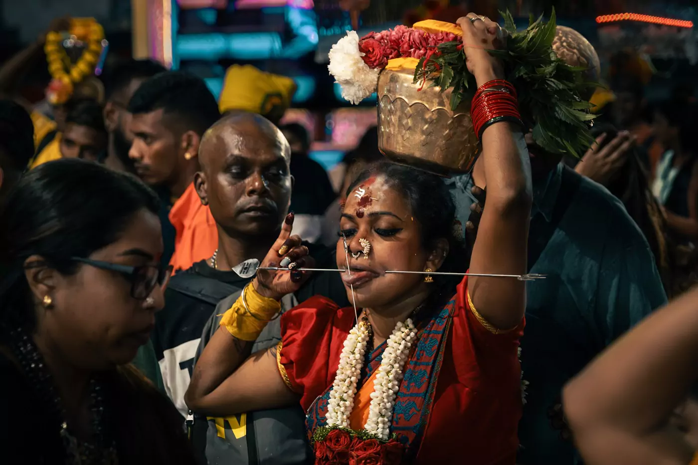 A devotee with multiple 'Vel' skewers in her face, holding a paal kudum (milk pot) offering to Lord Murugan on her head.