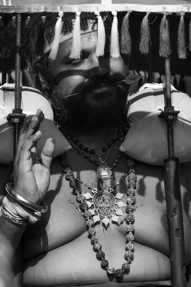 A serene looking kavadi wearer with a spear through their tongue standing in the sun during Thaipusam at Kuala Lumpur's Batu Caves.