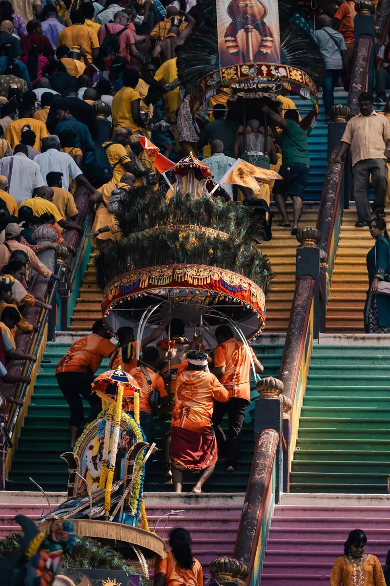 An entourage wearing orange helping their kavadi bearer up the steep stairs at the Batu Caves during Thaipusam.