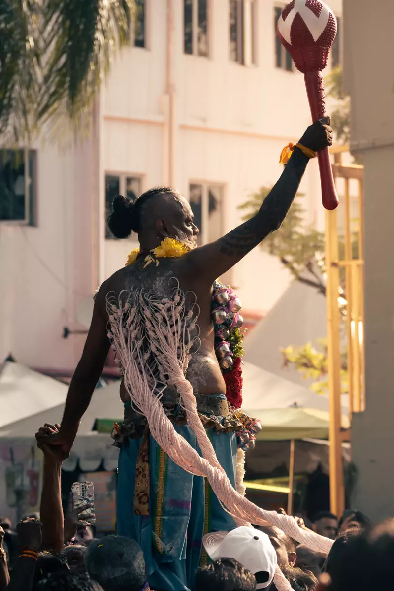 A person with dozens of hooks in their back holding aloft a red and white mace during the procession to the Batu Caves at Thaipusam.