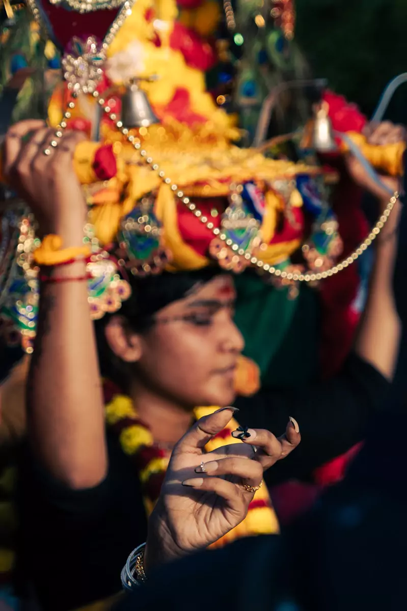 A manicured hand covered with intricate decorations with a kavadi wearer in the background.