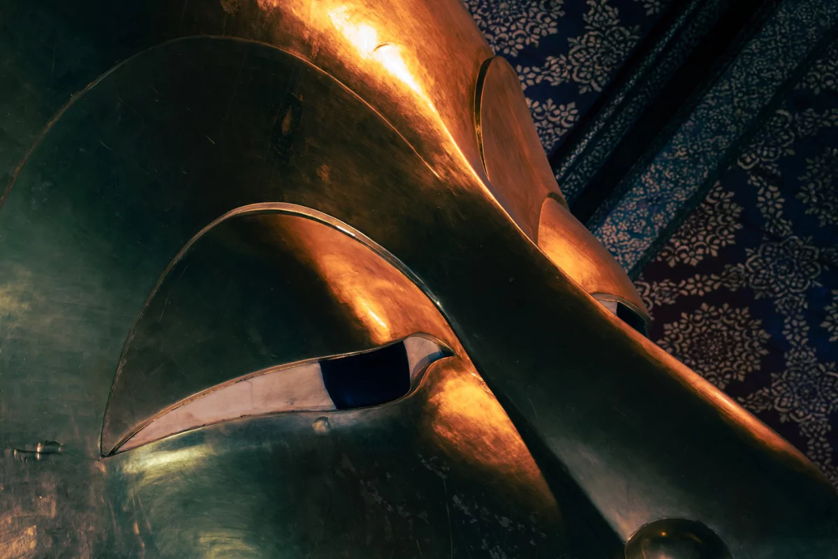 A giant golden head of Buddha in a temple in Bangkok with eyes partially closed.