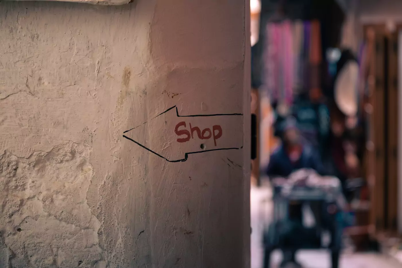 An arrow drawn on a wall in the medina of Tangier saying 'shop' in English, written in red pen.