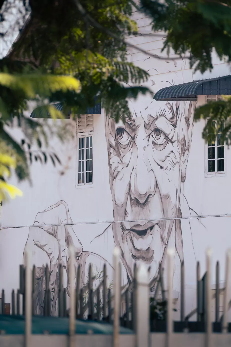 One of the famous street art pieces by Ernest Zacharevic in Ipoh, Malaysia. The mural on the side of a white building features an old man (uncle) drinking coffee.