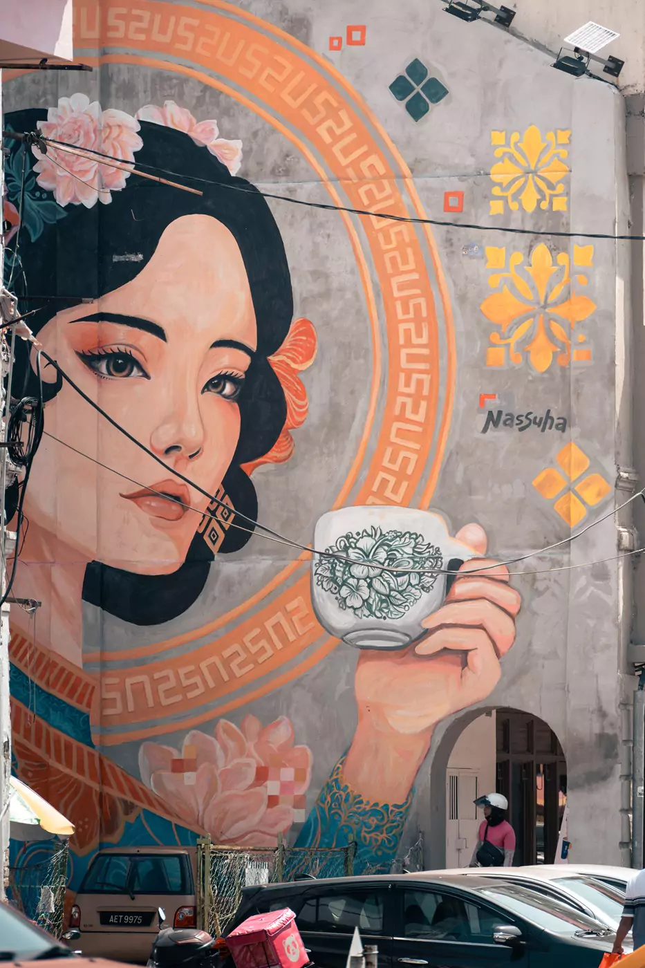 A huge, building high, mural in Ipoh, Malaysia of a woman drinking tea. The white teacup in her hand has an intricate floral design on it.