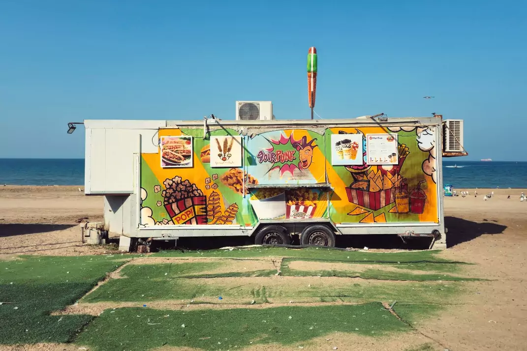 A food truck beside fake grass on the sand at Ghubrah Beach, Muscat.