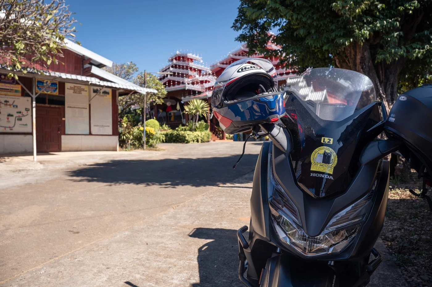 A motorcycle parked at a Burmese temple with a motorcycle helmet on a handlebar.