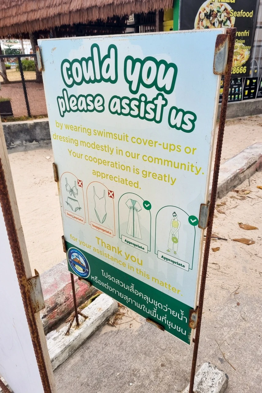 A sign by the beach informing visitors to not wear beach clothing when wandering through a local community on Koh Yao Yai.