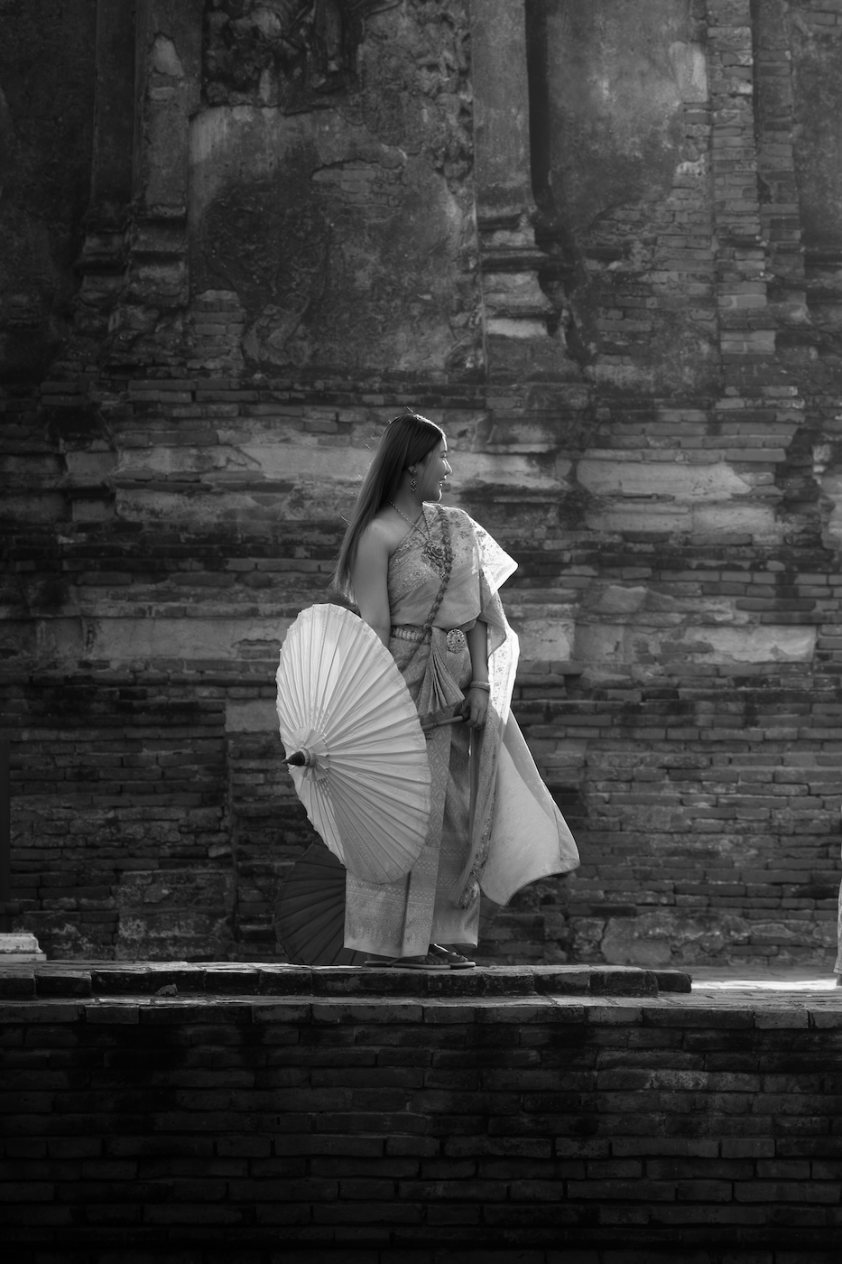 Black and white photo of a woman posing for a photo, with an umbrella as a prop, at Wat Chaiwatthanaram temple in Ayutthaya.