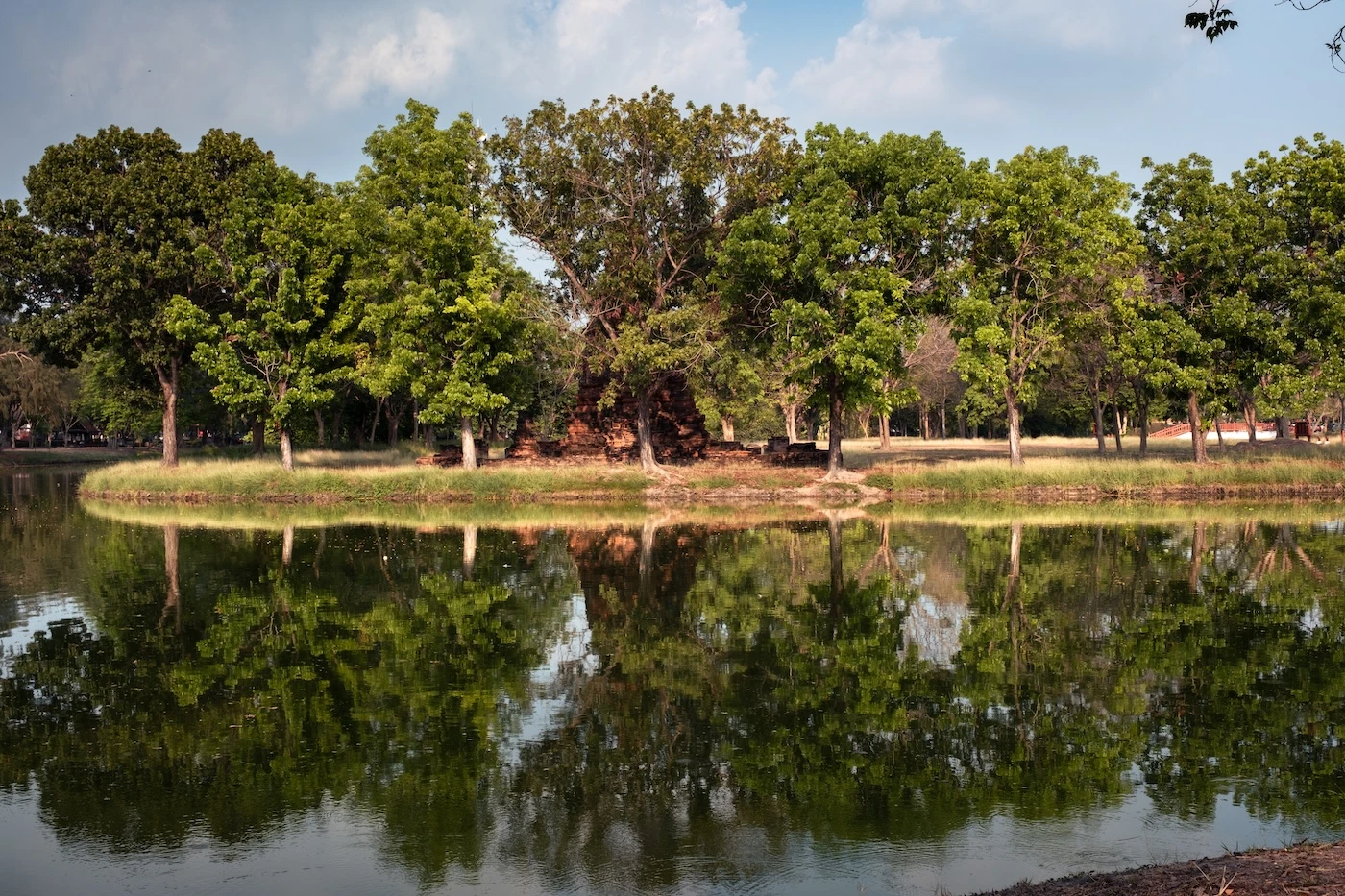 Reflections of a chedi and trees in the water of a lake at Bueng Phra Ram Park in Ayutthaya.