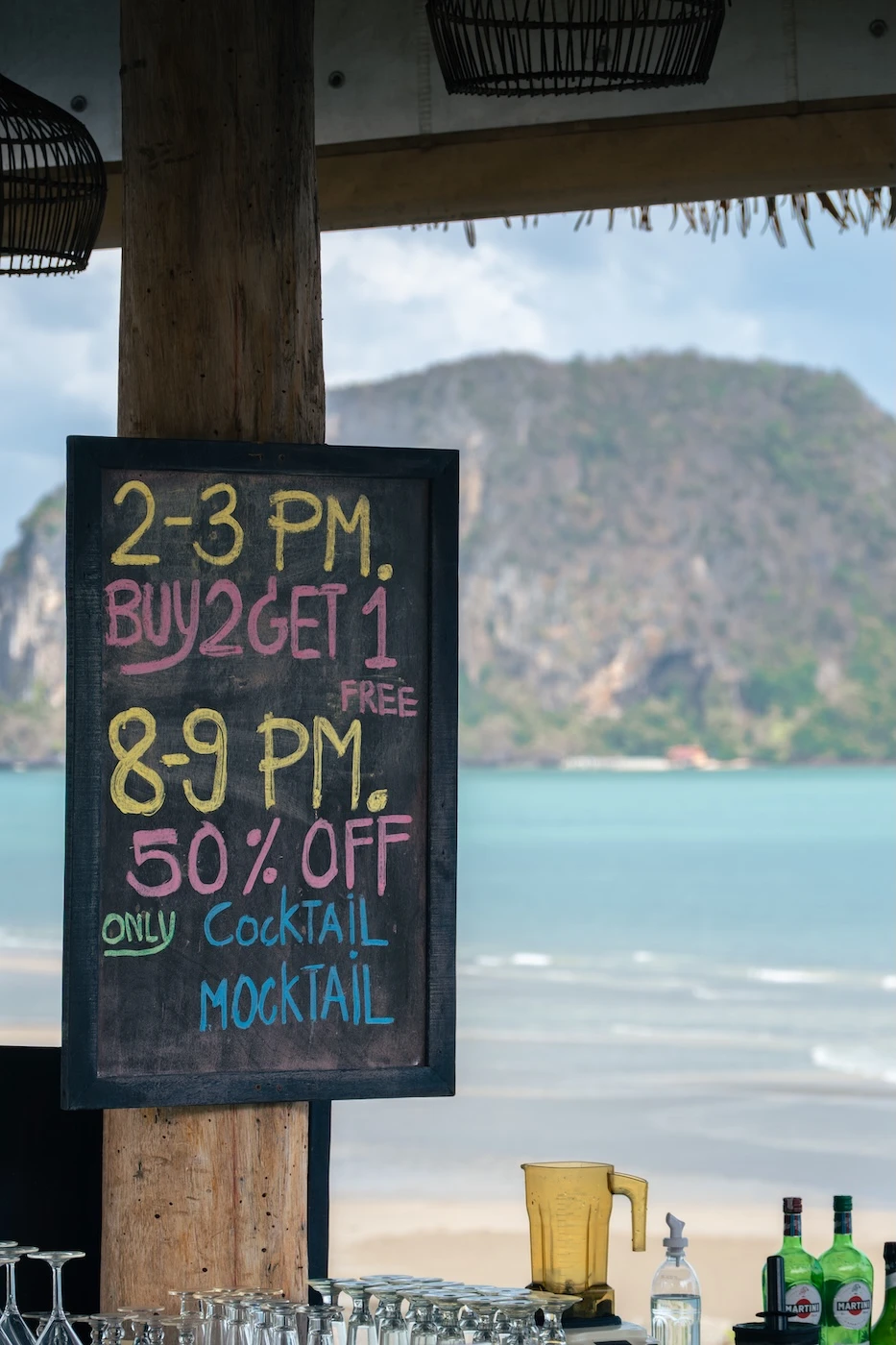 A board advertising drinks deals at a hotel saying "2-3 PM buy 2 get 1 free. 8-9 PM 50% off only cocktails and mocktails"