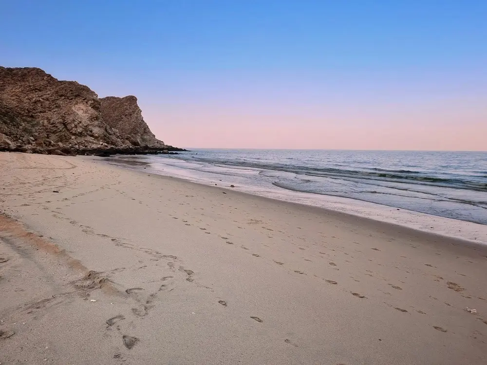 Footsteps along the sandy shore of As Siffah Beach.
