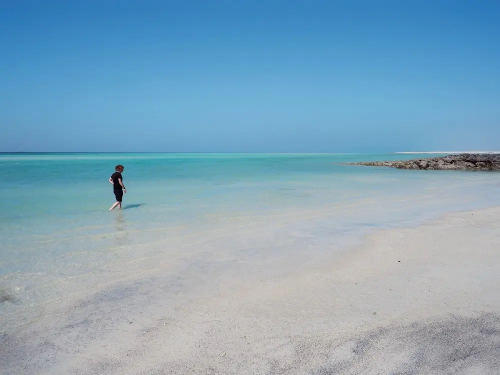 A person walking in the shallows of a sandy stretch of Ghab Beach on Masirah Island.