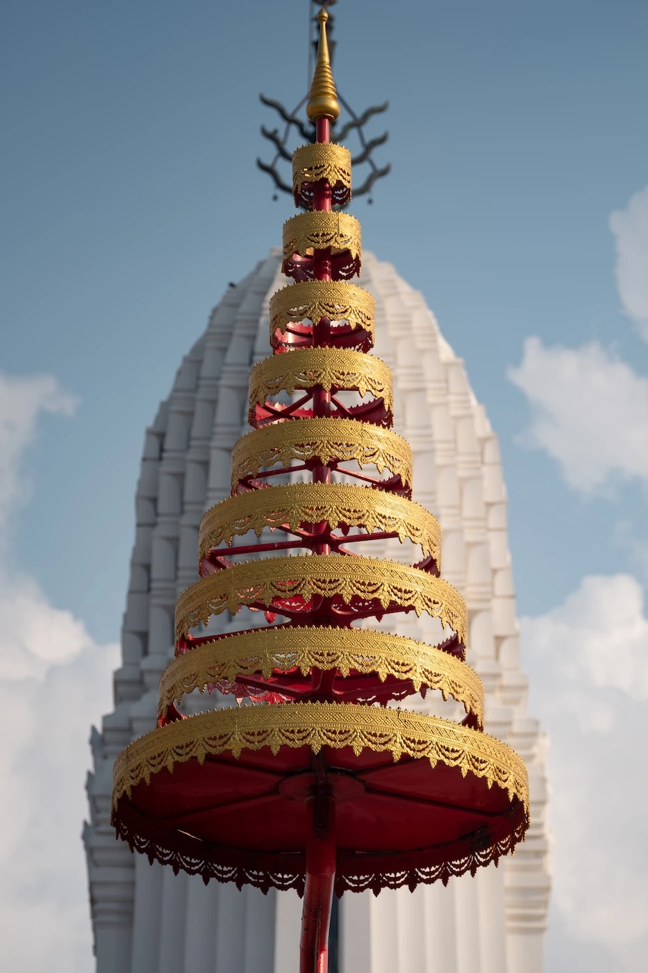 Multiple layers of a golden umbrella with a gleaming white prang tower in the background at Wat Phutthaisawan temple.
