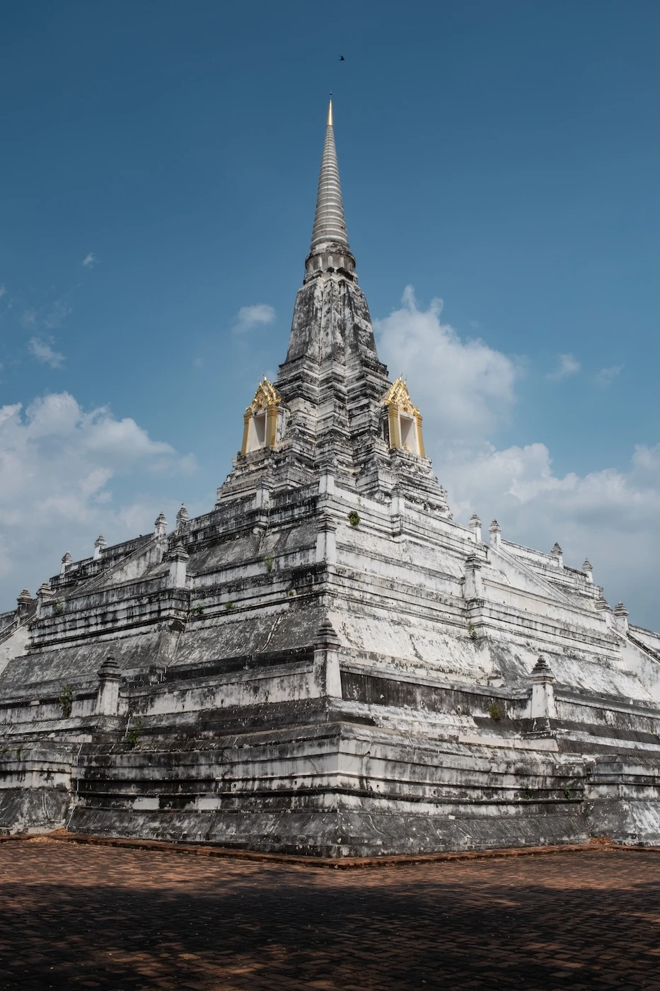 Ruins of a large white coloured stupa on a platform with stairs leading up to it.