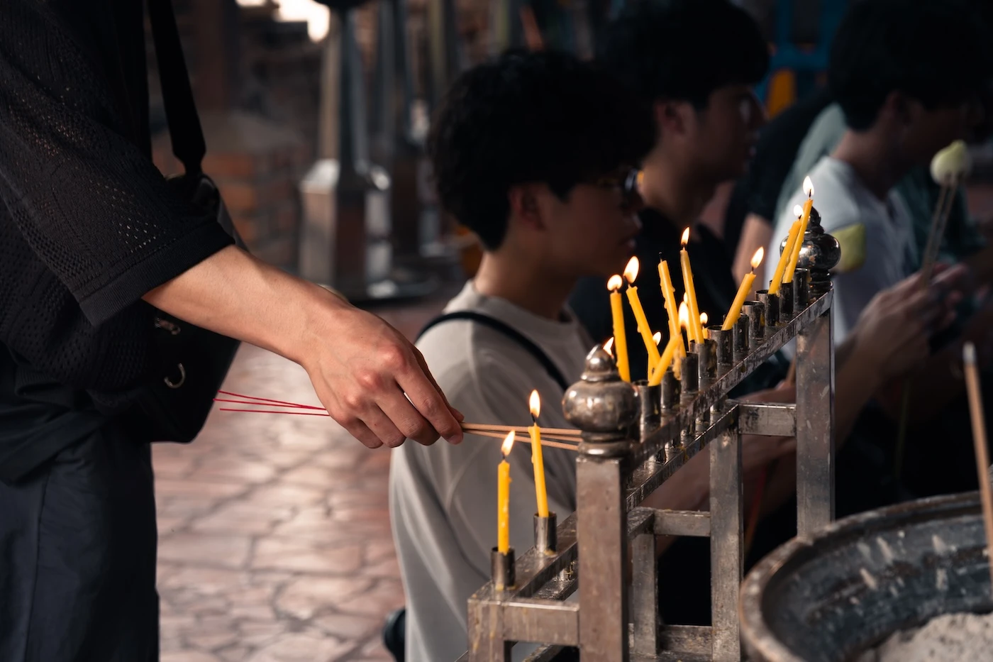 A person lighting incense sticks with a candle at a temple shrine at Wat Yai Chai Mongkol.
