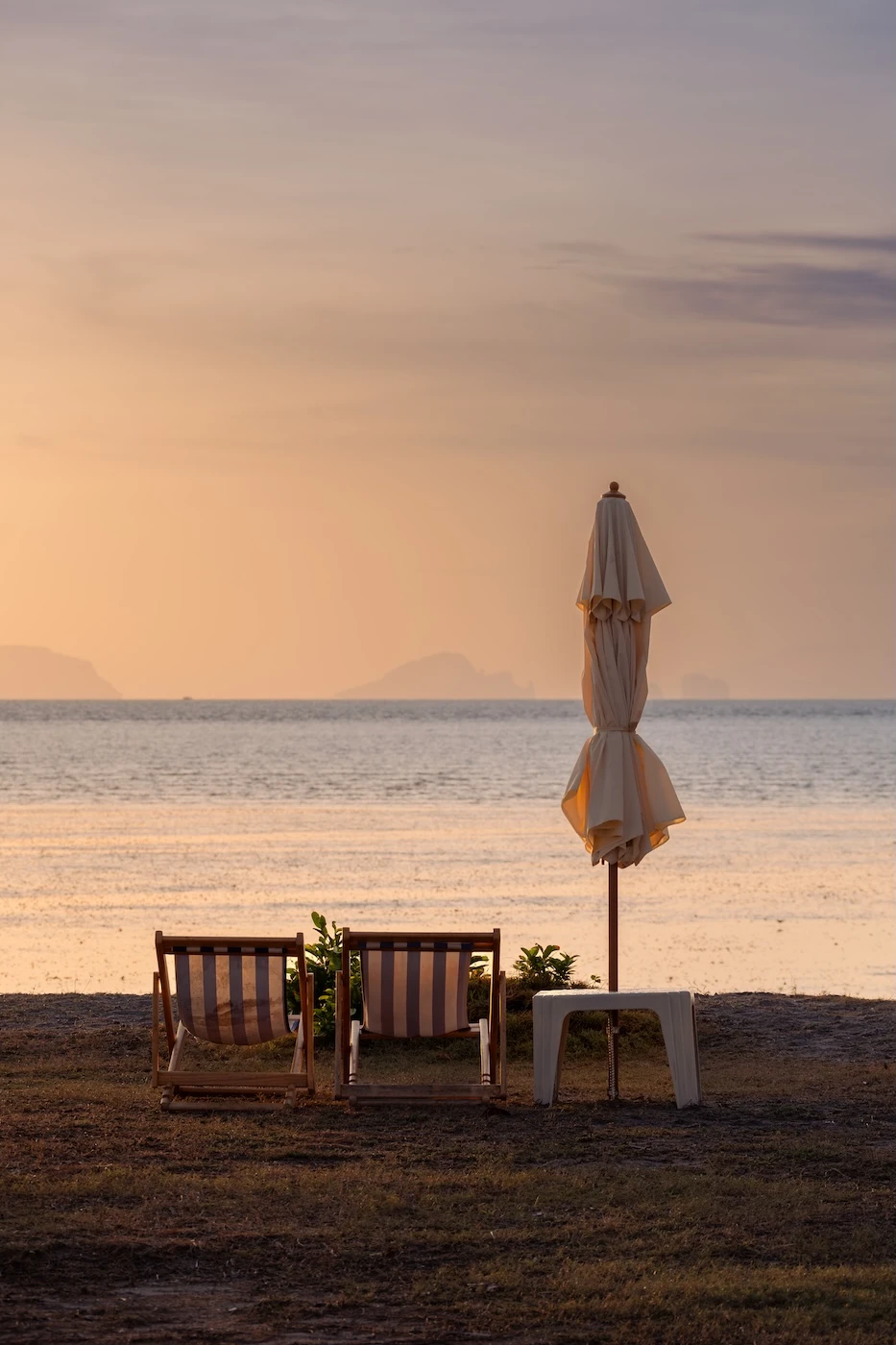 A duo of deckchairs and a white parasol set up by the beah on Koh Yao Yai, Thailand.