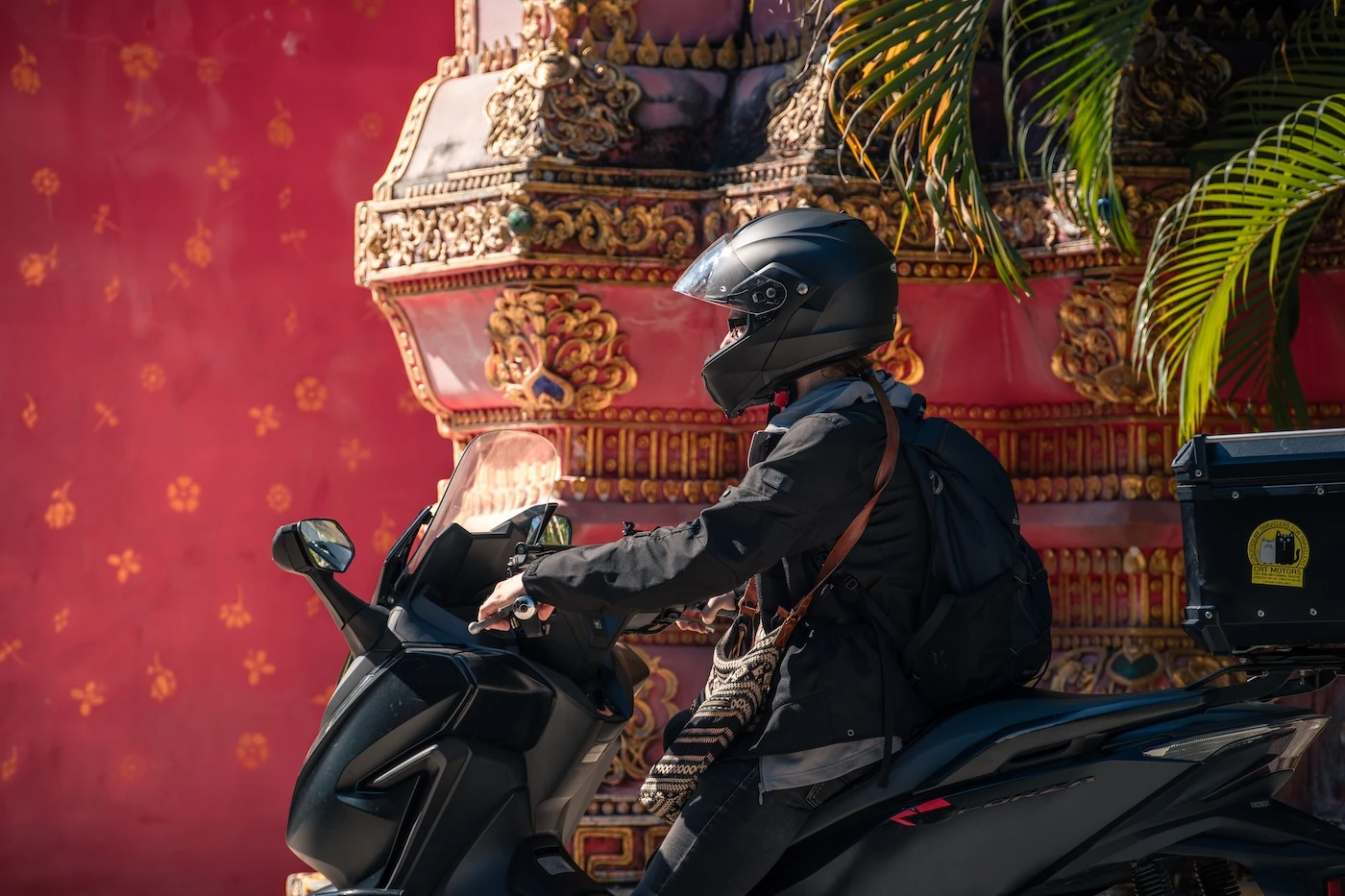 A motorcyclist wearing a black helmet stopped outside a temple with colourful walls near Pai.