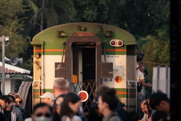 The Kanchanaburi train travelling over the bridge over the river Kwai which is full of tourists.
