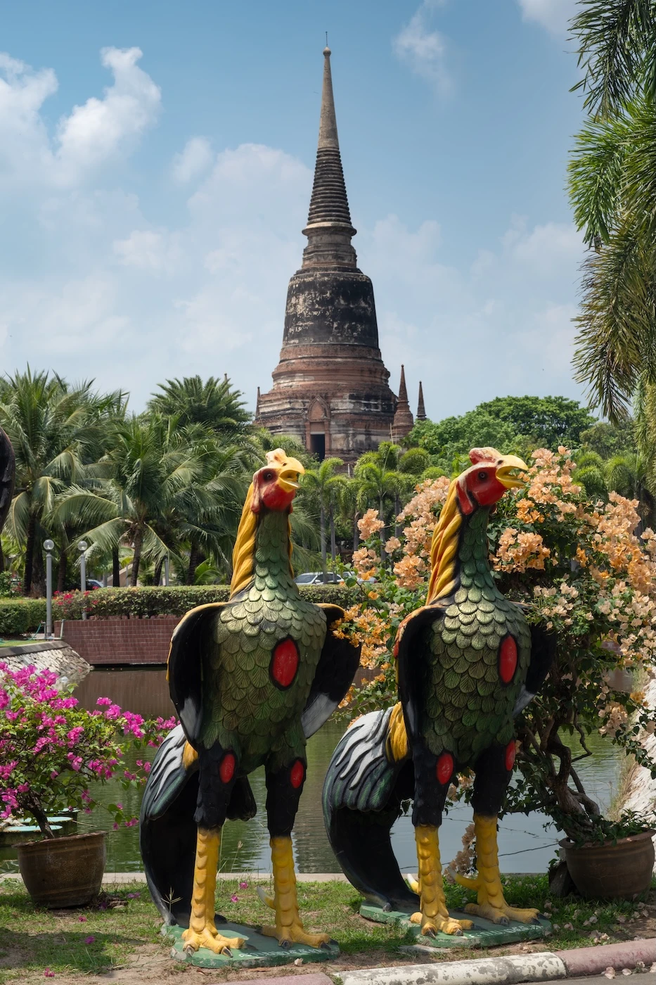 Two rooster statues stood in green,red, black and yellow beside a lake at Wat Yai Chai Mongkol Worawihan, Ayutthaya.