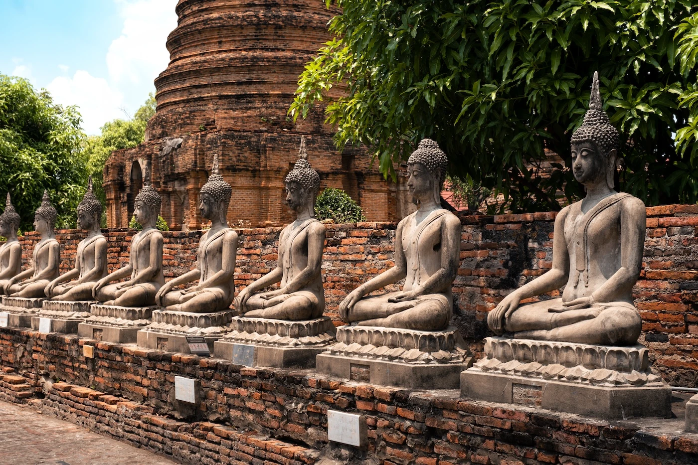 A row of seated stone Buddhas by a wall at the Buddhist temple of Wat Yai Chai Mongkol Worawihan in Ayutthaya.