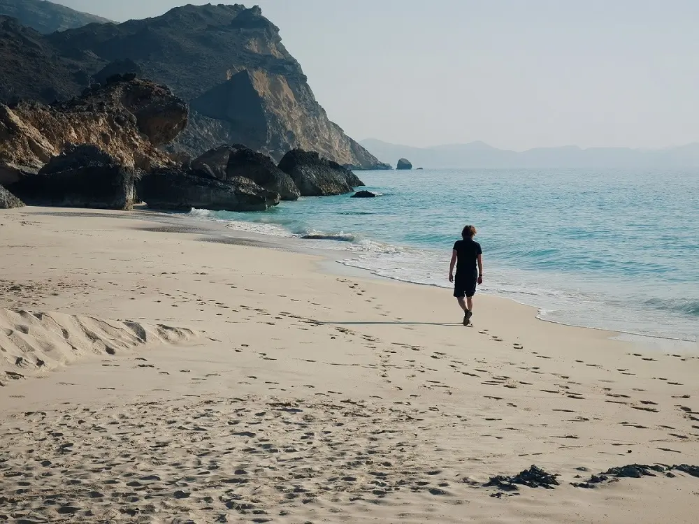 A person taking a stroll along the sandy shoreline of Fazayah Beach near Salalah, Oman.