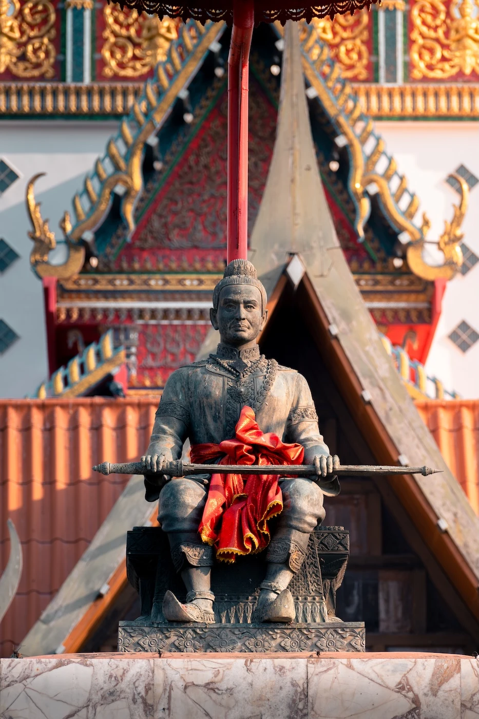 A statue of a King U-Thong sitting beneath an umbrella, located atop a wall outside Wat Phutthaisawan temple.