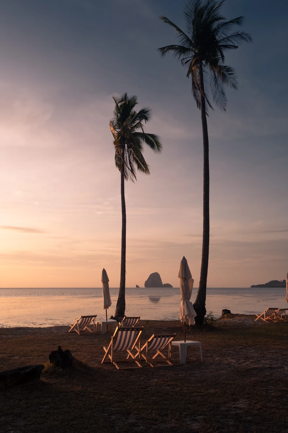 Sunrise at Laem Haad Beach in Koh Yao Yai with the sun lighting up the beach chairs and parasols near the water's edge.