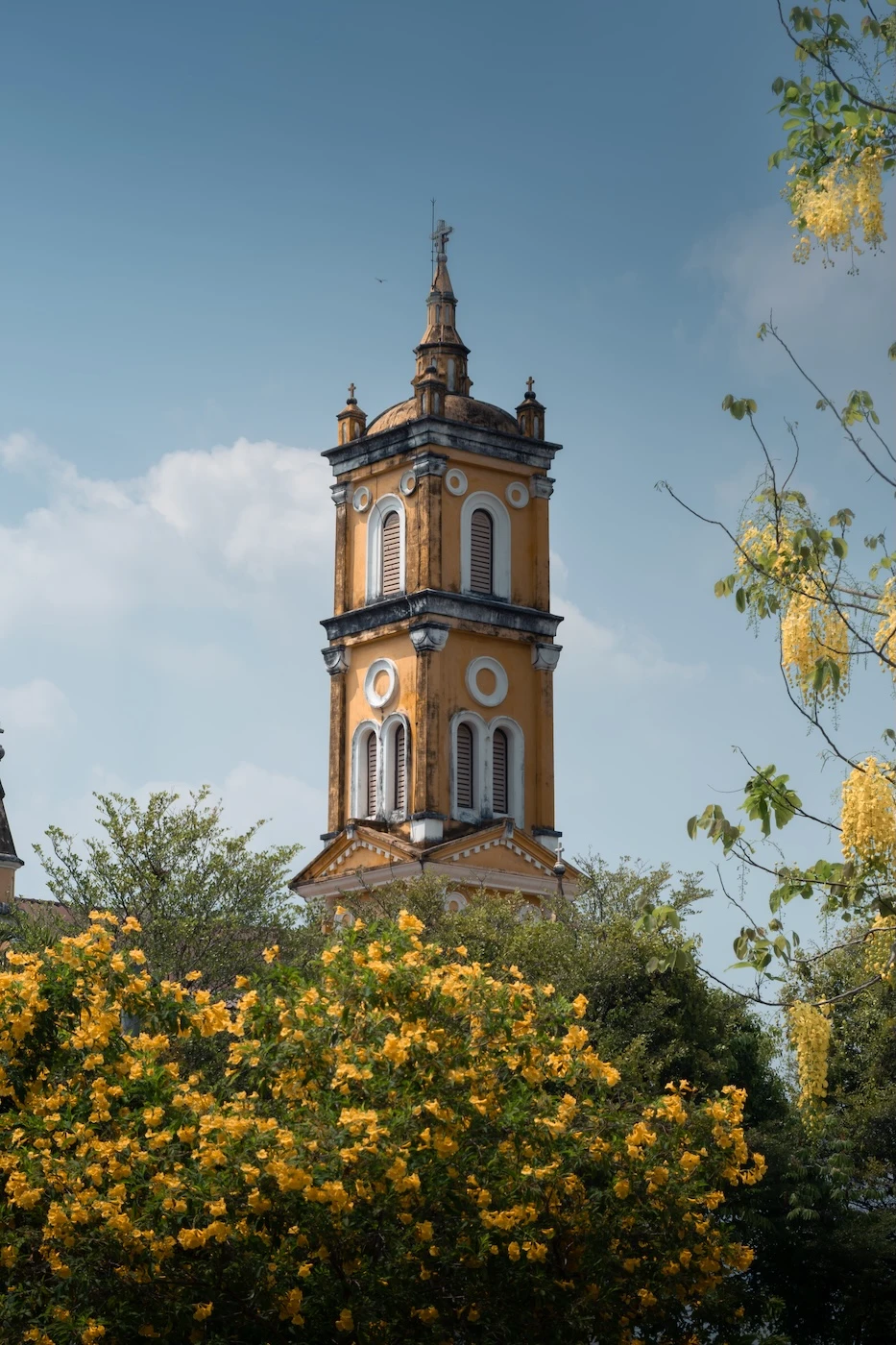 Vibrant yellow tower at St. Josephs Church, towering over yellow flowers in the garden.