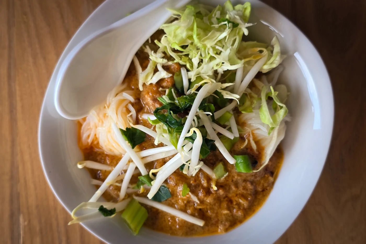 A bowl of local thai food in a white bowl, served with fesh salad.