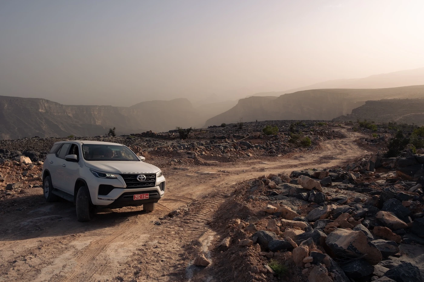 A white rental 4WD vehicle stopped on a dirt track while driving off-road through Jebel khdar in Oman.