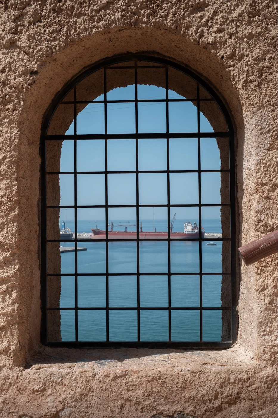 A ship in the port at Muscat's Mutrah seen through a curved window at the Mutrah Fort.