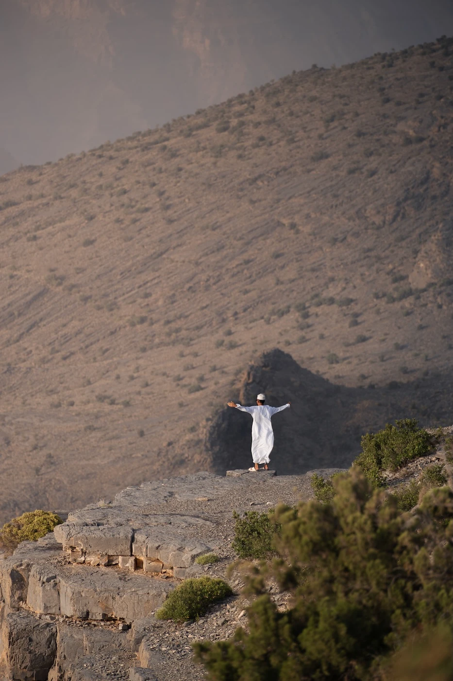 A visitor to the Hajar Mountains posing for a photograph along the cliff edge.