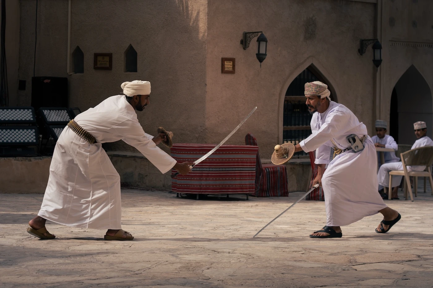 Two people play sword fighting using ancient Omani weapons including swords and bucklers, in the courtyard of Nizwa Fort.