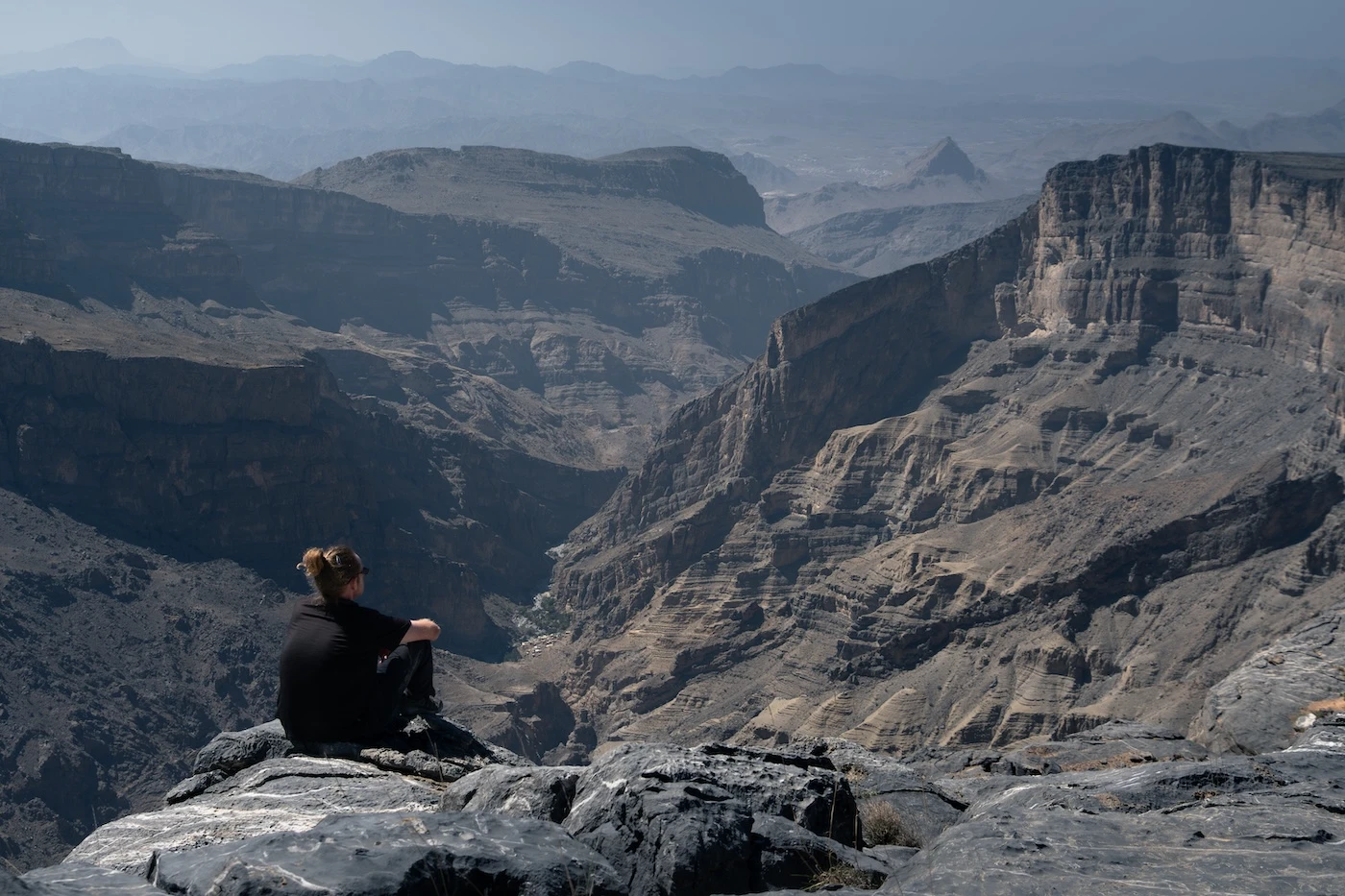 A person sat along a mountain ridge on the w19 walk in Jebel Akhdar, Oman.
