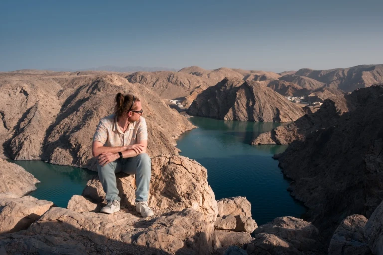 A person sat atop a cliff edge overlooking deep-blue waters by the coastline at a viewpoint at Yenkit Bay in Muscat, Oman.