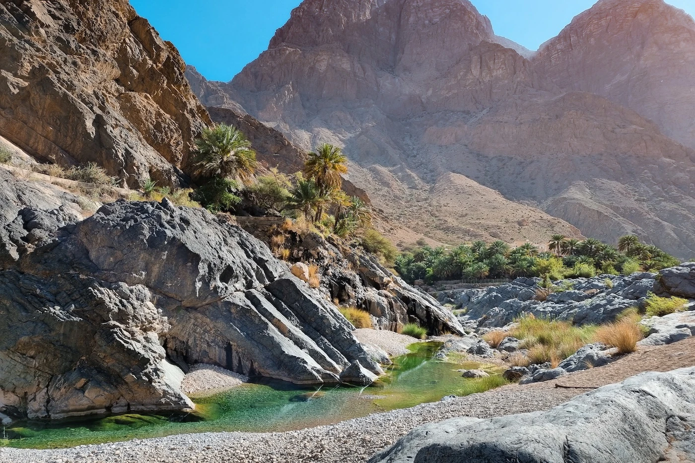 A clear pool of blue-green water at the base of a rockwall at Wadi Al Arbeieen in Oman's Eastern Hajar Mountains.