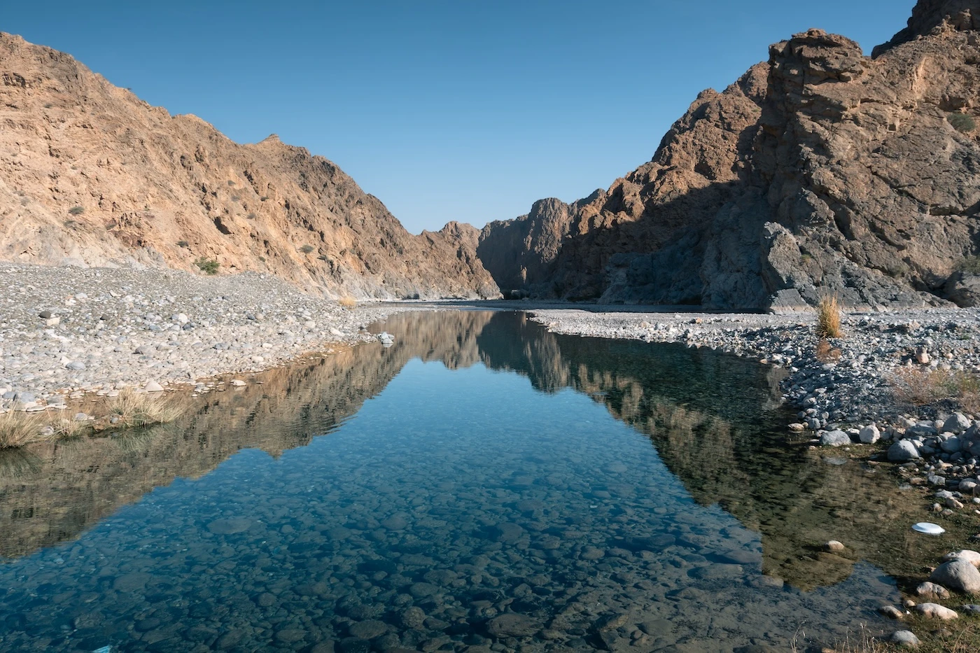 Clear waters at the bottom of Wadi Dayqah reflecting the surrounding valley scenery.
